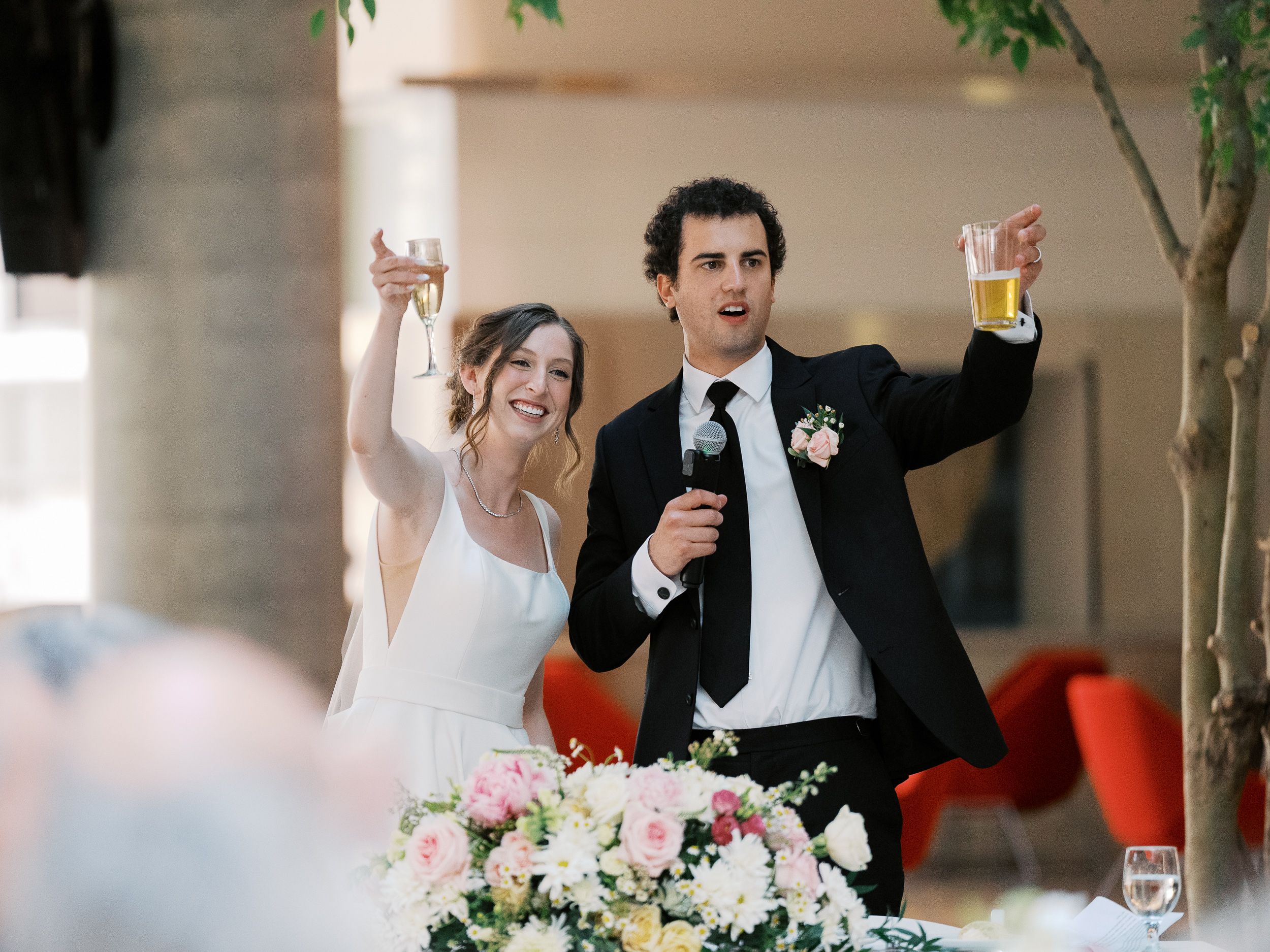 Wedding guests raise their glasses in a toast at an elegant indoor reception celebration.