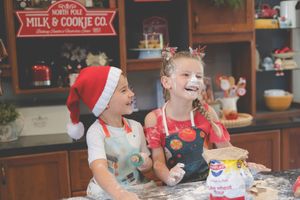 Siblings in Christmas themed setup baking with flour on their noses and laughting at each other.