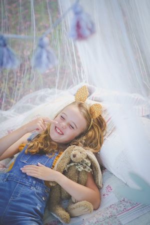 An Easter scene with a yound girl lying in a netted tent cuddling her stuffed bunny