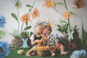 Siblings in a easter setup holding a basket with carrots in and sitting amongst easter decorations