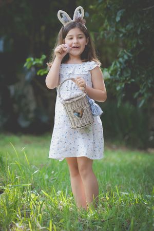 An Easter image of a girl having found an easter egg holding it and a basket in her hand and surprised look on her face.
