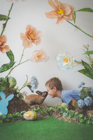 A boy leaning toward a real bunny giving him a kiss on his nose with an easter garden background