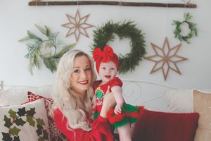 Mom and babe smiling at the camera close together, dressed in Christmas colours and a background of Christmas wreaths