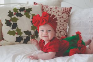 A toddler in cute christmas outfit lying on a bed decorated with Chirstmas cushings smiling at the camera