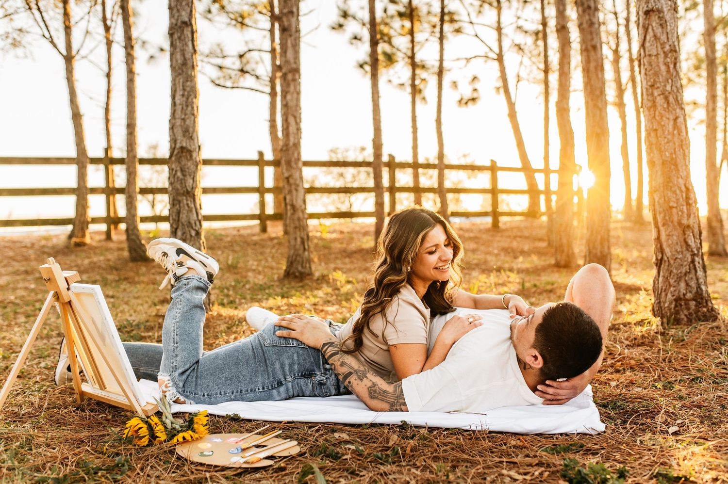 A couple relaxing on a blanket among pine trees at sunset.
