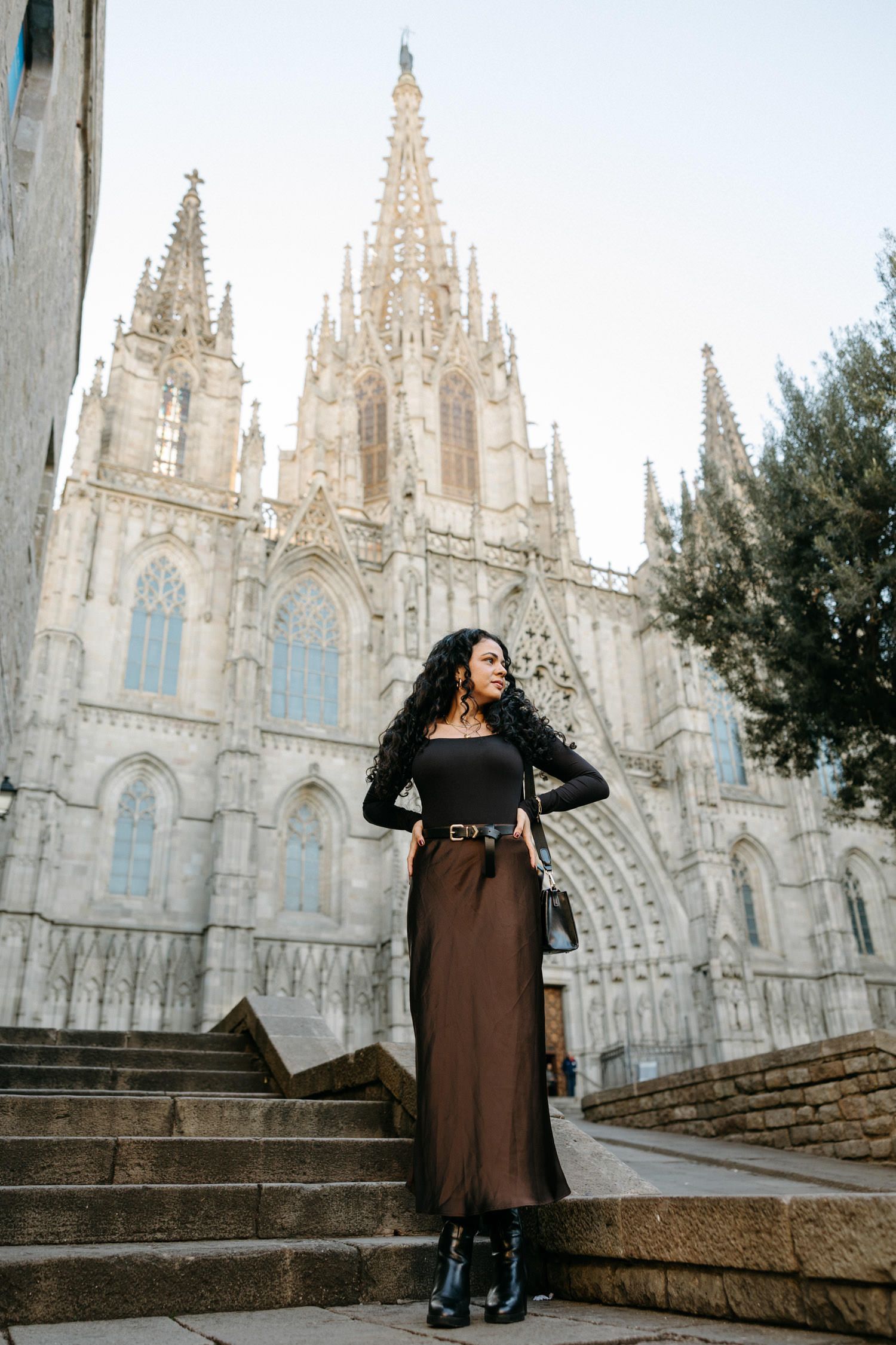 Woman in black coat poses on steps before stunning Gothic cathedral with white spires.