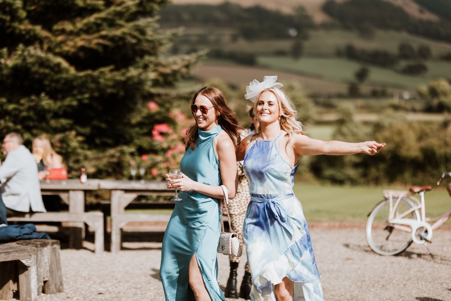 Two people in blue outfits celebrate outdoors in a scenic mountain setting with picnic tables and a bicycle in background.