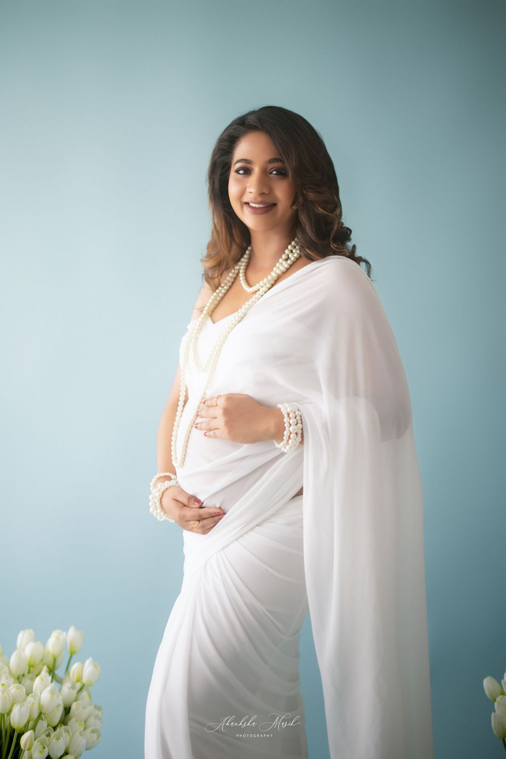 Maternity photo series in white fabric against blue backdrop with elegant white tulips in final frame.