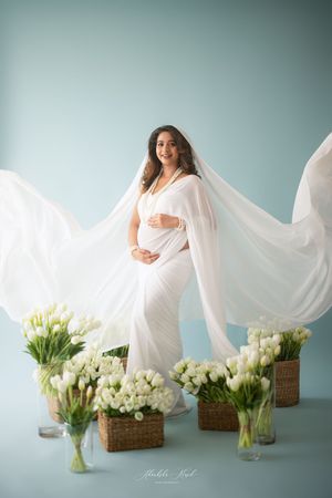 Artistic maternity photo series with flowing white fabric and elegant white tulip bouquets against a blue backdrop.