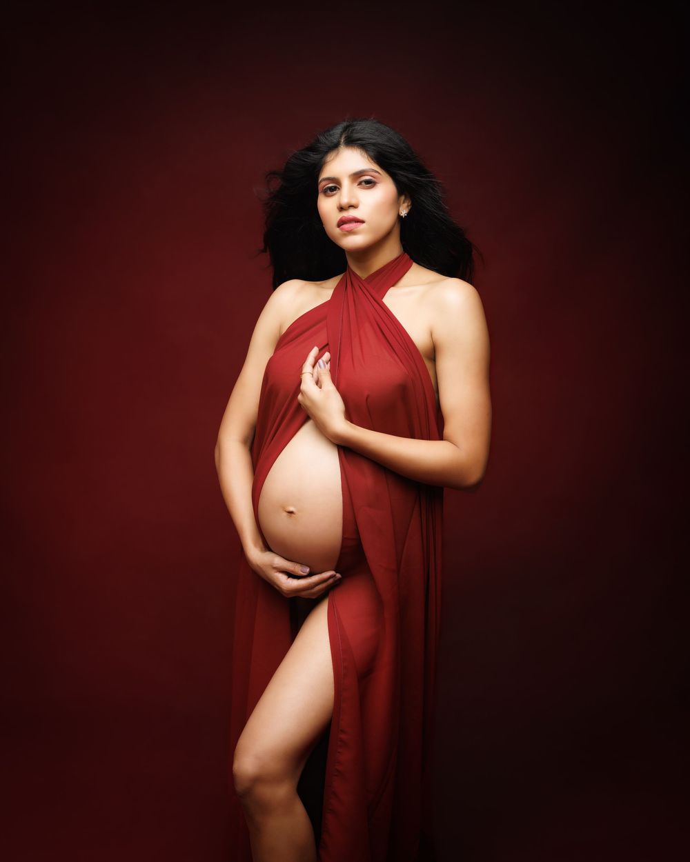 A series of artistic maternity portraits showing a pregnant woman in a flowing burgundy dress against a dark background.