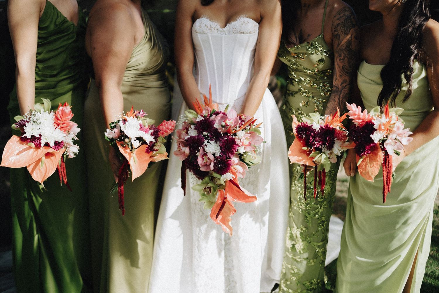 Wedding party group walks on a tropical beach with palm trees wearing flowered leis and beachwear in Hawaii.