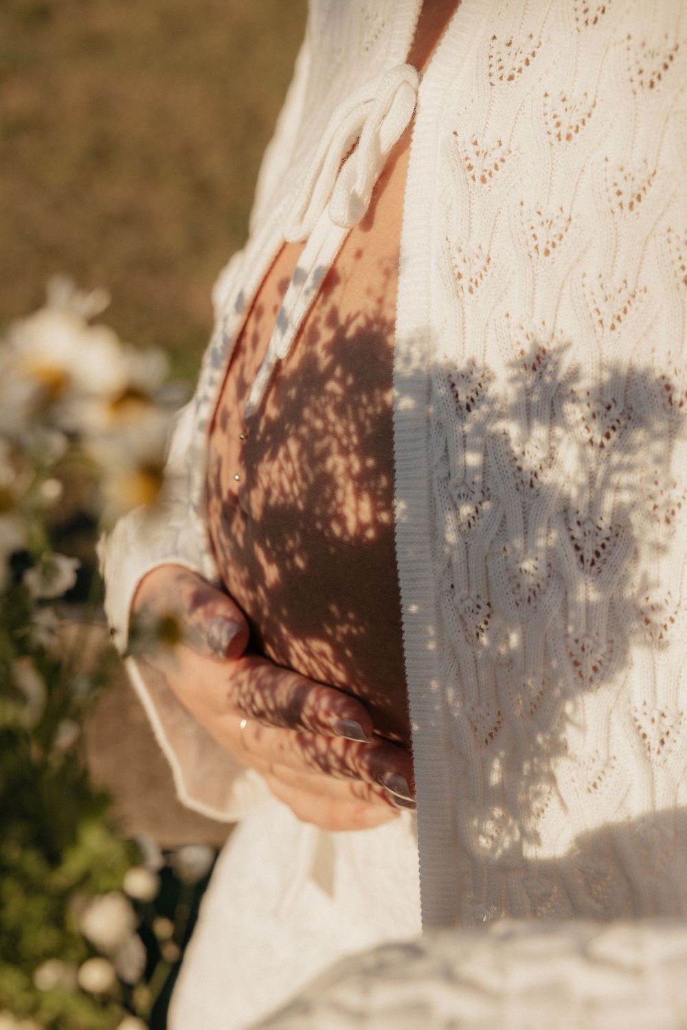 Delicate lace fabric casts intricate shadow patterns on a pregnant belly in warm sunlight.