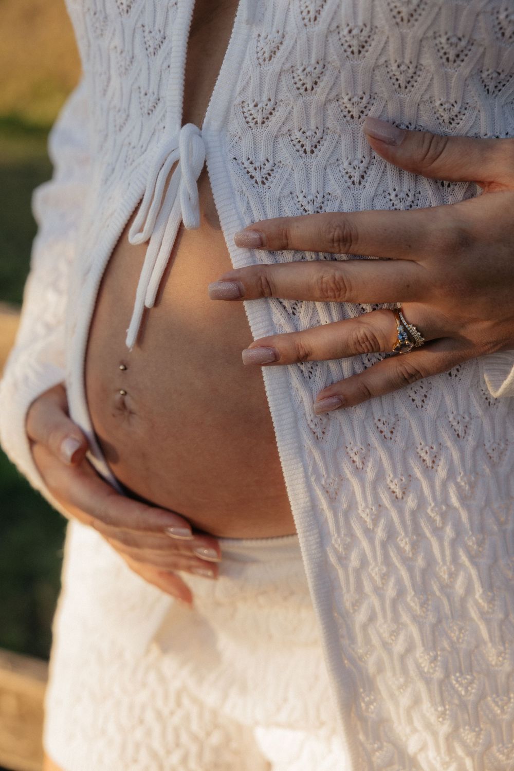 Close-up sequence of hands touching a pregnant belly in a white lace dress.