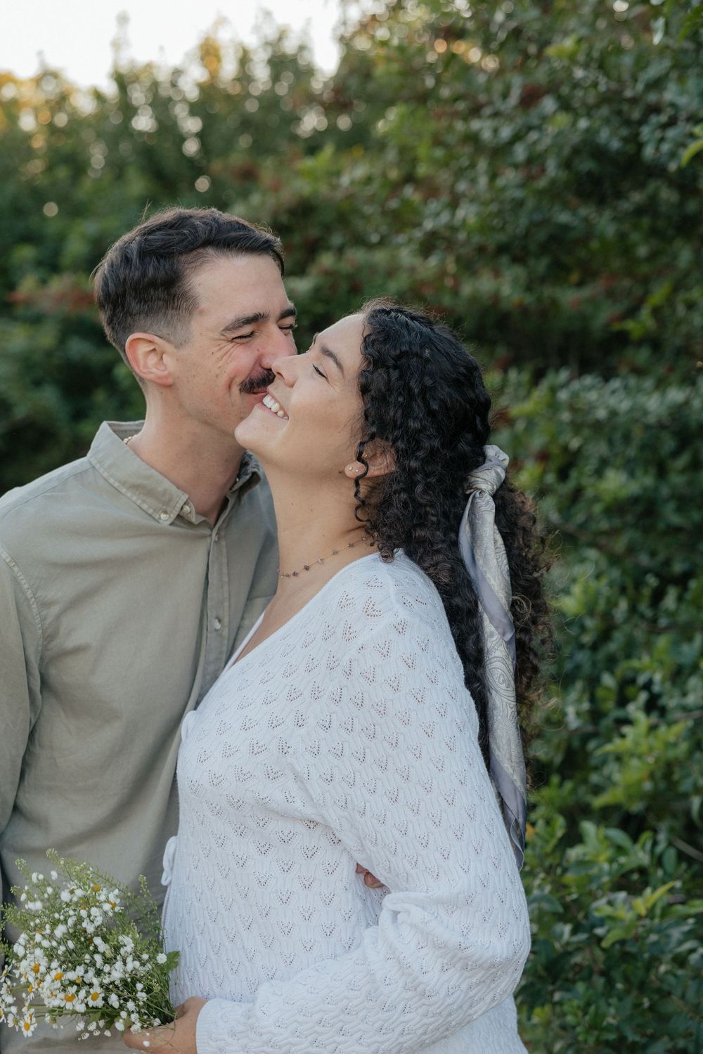 Romantic outdoor couple sharing tender moments against a green garden backdrop.