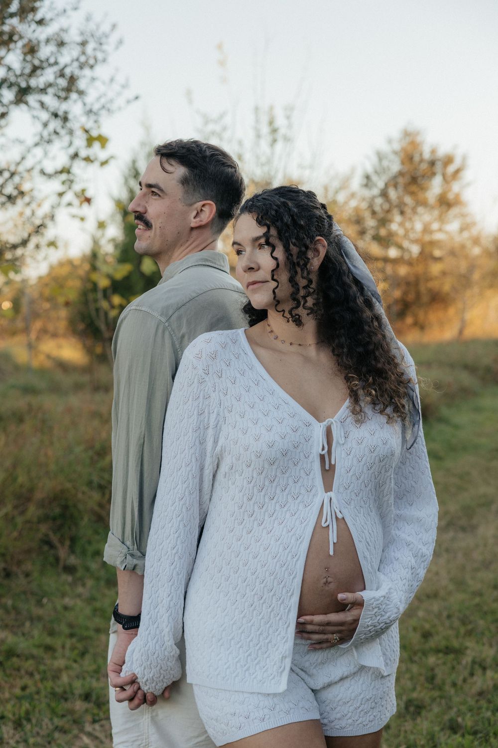 A couple embraces in a romantic outdoor photoshoot during golden hour in a natural field setting.