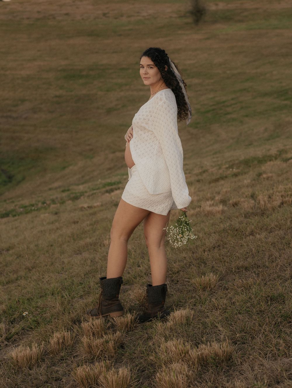 A person in a white sweater walks across a grassy hillside on an overcast day.