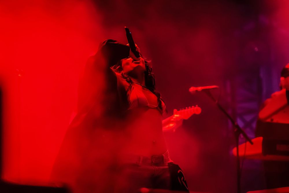 Red and purple lighting creates a moody atmospheric glow in a dark nightclub or concert venue scene.