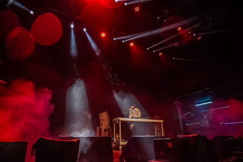 Dramatic concert stage lit with red lights and fog while a performer plays at an illuminated piano setup.