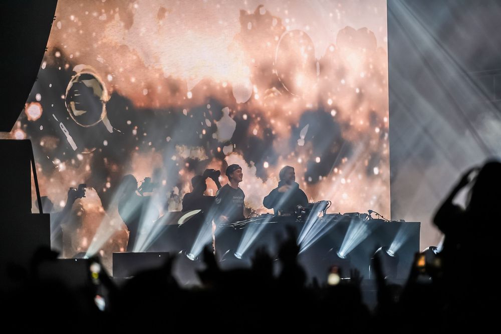 Music festival audience in silhouette with pink atmospheric lighting and dramatic smoke effects.