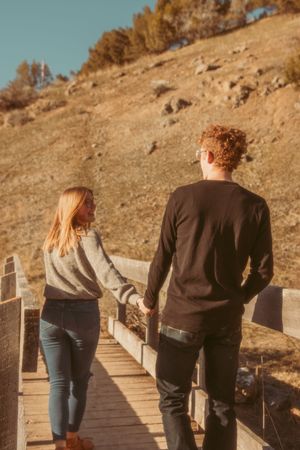 A couple holding hands while walking together on a wooden boardwalk trail on a sunny autumn afternoon.