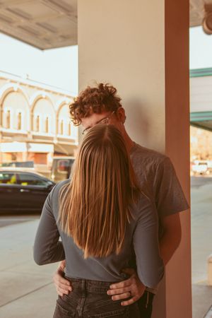 A couple embraces in an intimate moment against a pillar on a city street at sunset.