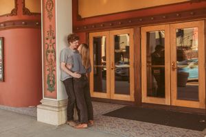 Vintage art deco movie theater entrance showcasing ornate red decorative columns and glass display cases in warm lighting.