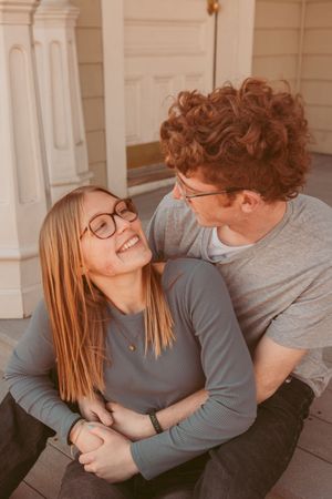 A couple shares a romantic moment on a front porch, leaning into each other and laughing together.
