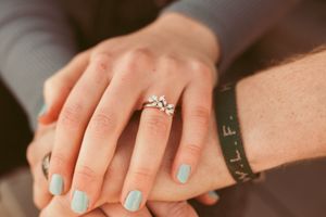 Close-up of hands wearing a sparkling diamond engagement ring with light blue nail polish and a black bracelet.