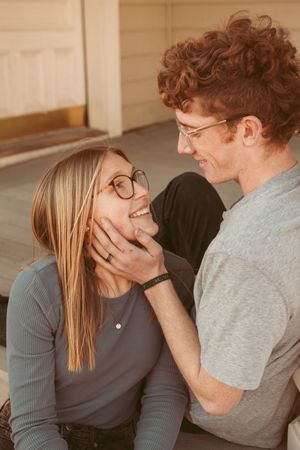 A couple wearing glasses share a tender moment while sitting together outdoors.