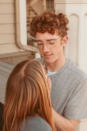 A tender romantic moment between a couple with one wearing glasses and a grey t-shirt in warm lighting.