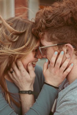 A romantic couple in glasses share an intimate moment with their hands on each other's faces.