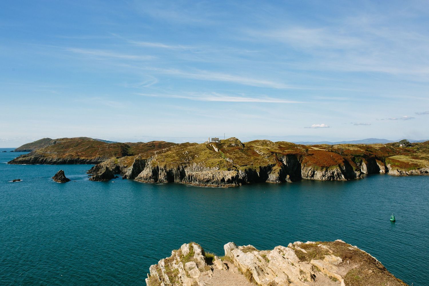Rocky coastal cliffs and turquoise waters along a rugged shoreline under bright blue skies in Wales.