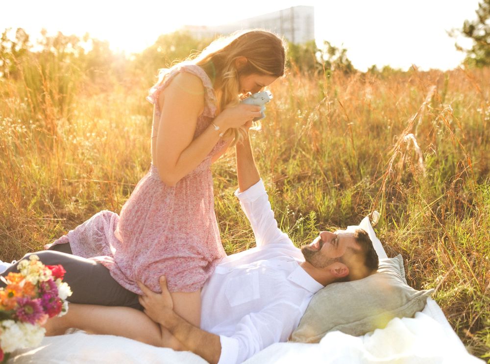 Romantic couple laughing together while laying on blanket in sunny meadow with flowers nearby.