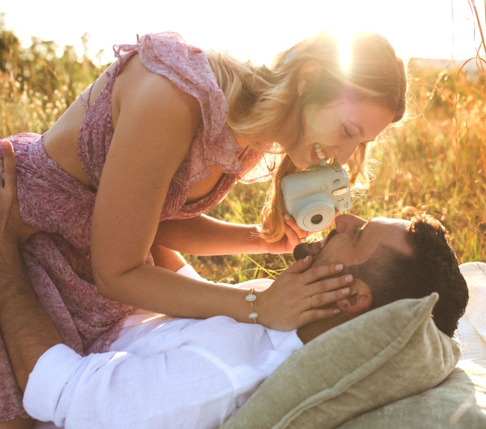Two romantic figures share an intimate moment in a sunlit golden meadow during sunset, lying in the grass together.