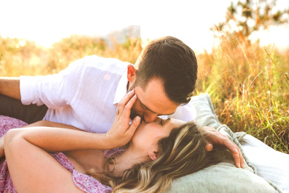 Affectionate couple lying in golden sunlit grass during golden hour sunset.