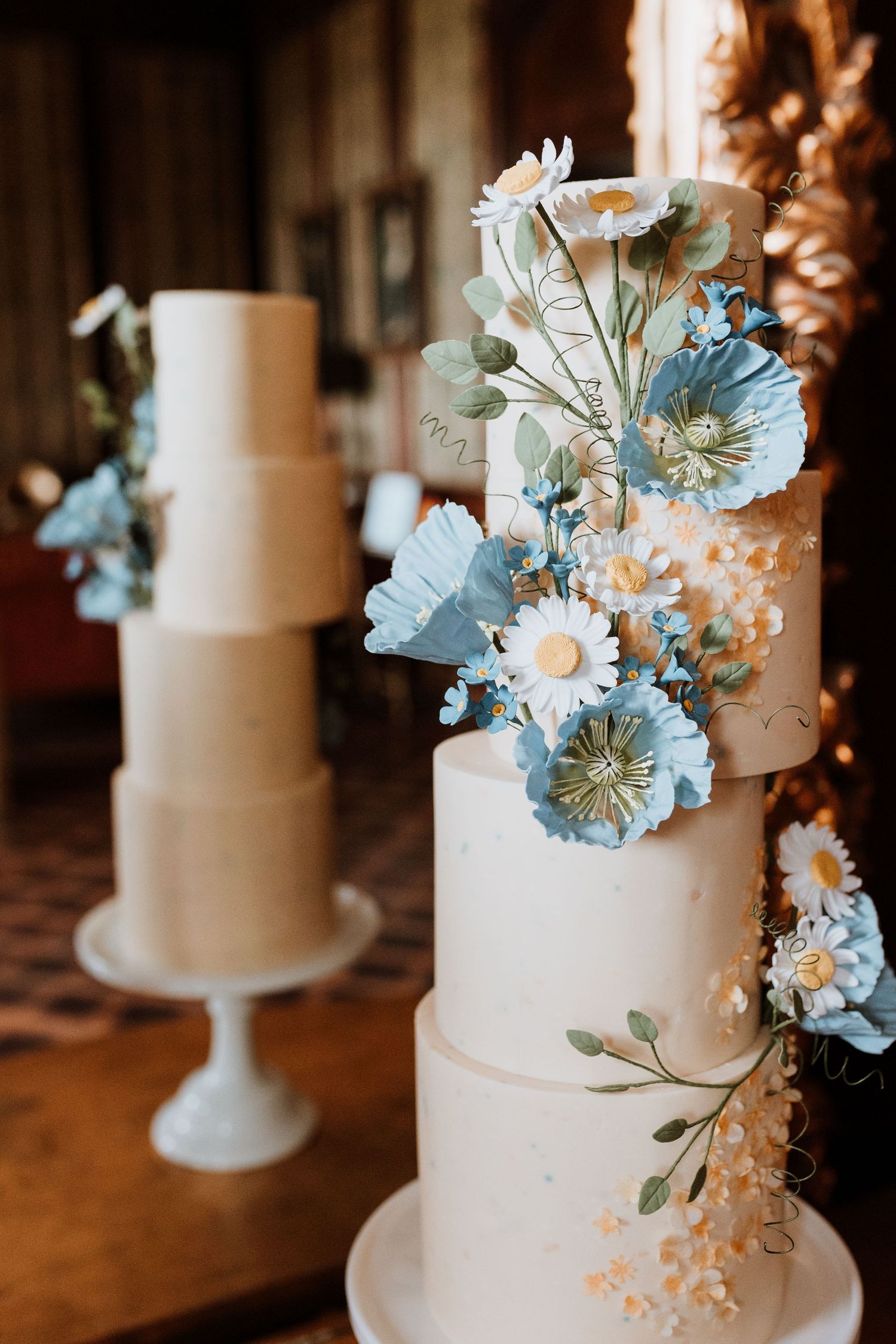 Elegant white multi-tiered wedding cake decorated with light blue and white sugar flowers in a romantic setting.