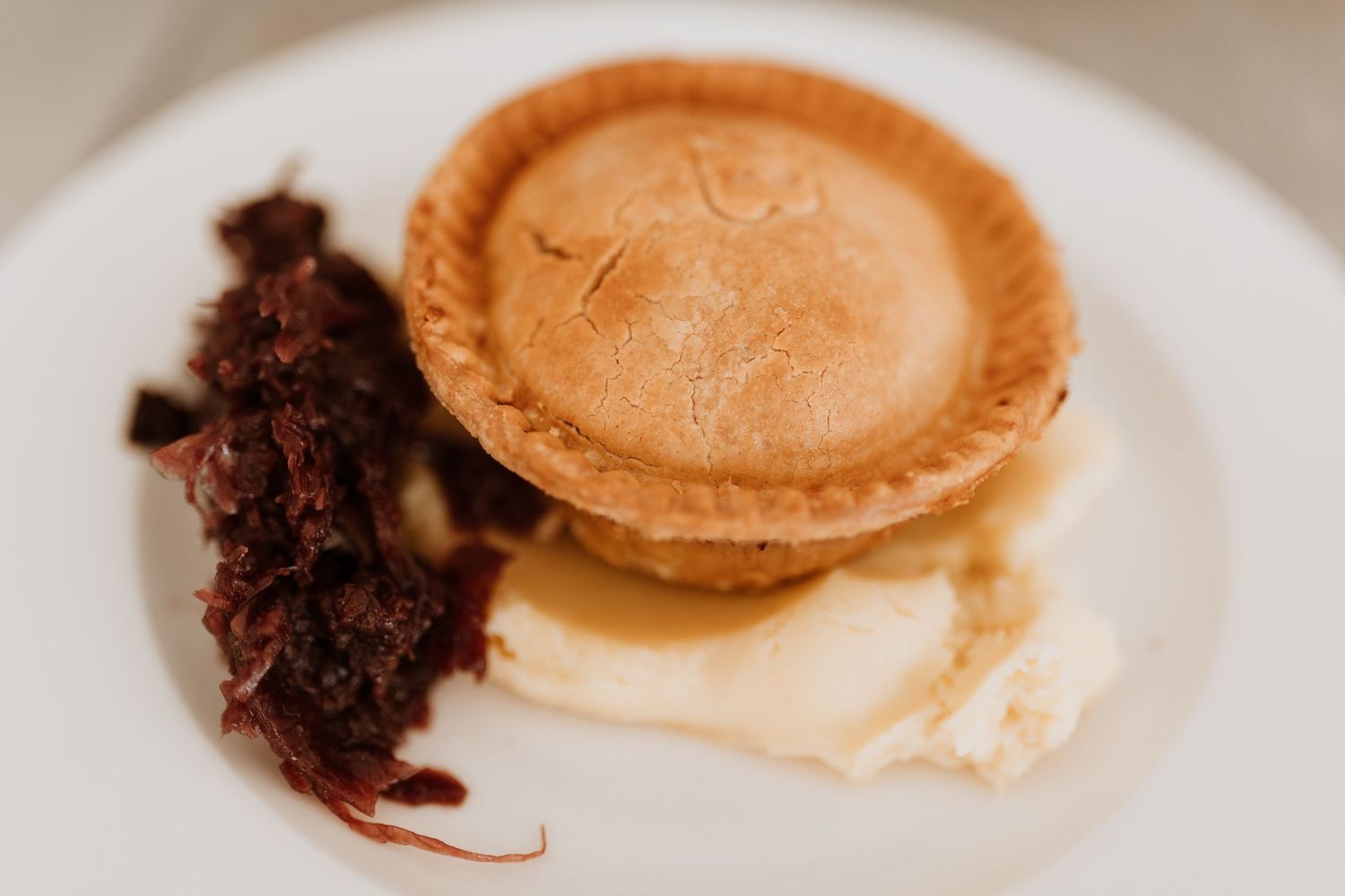 A small round pie served on a white plate with mash and cabbage