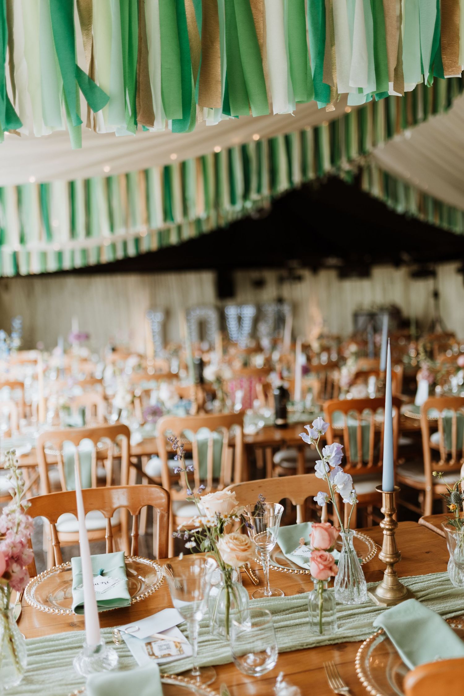 Elegant wedding reception tables set with candles and floral centerpieces under green and white streamers hanging from ceiling.