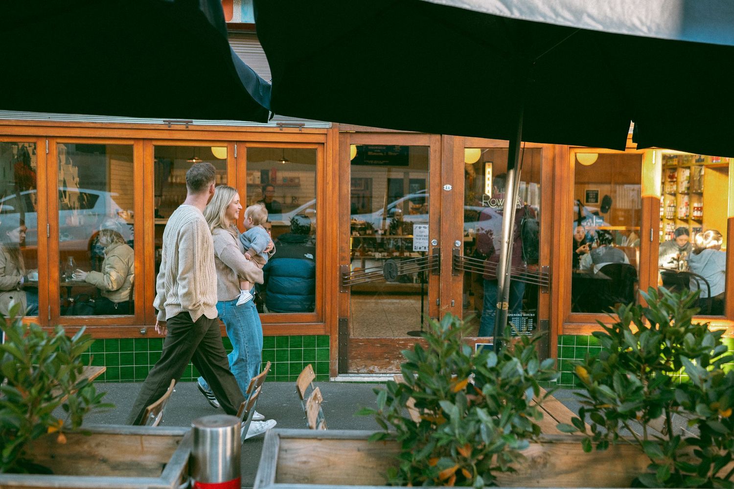 Family walking past a café in Richmond during a documentary-style neighbourhood photo session, with parents chatting and baby in arms.