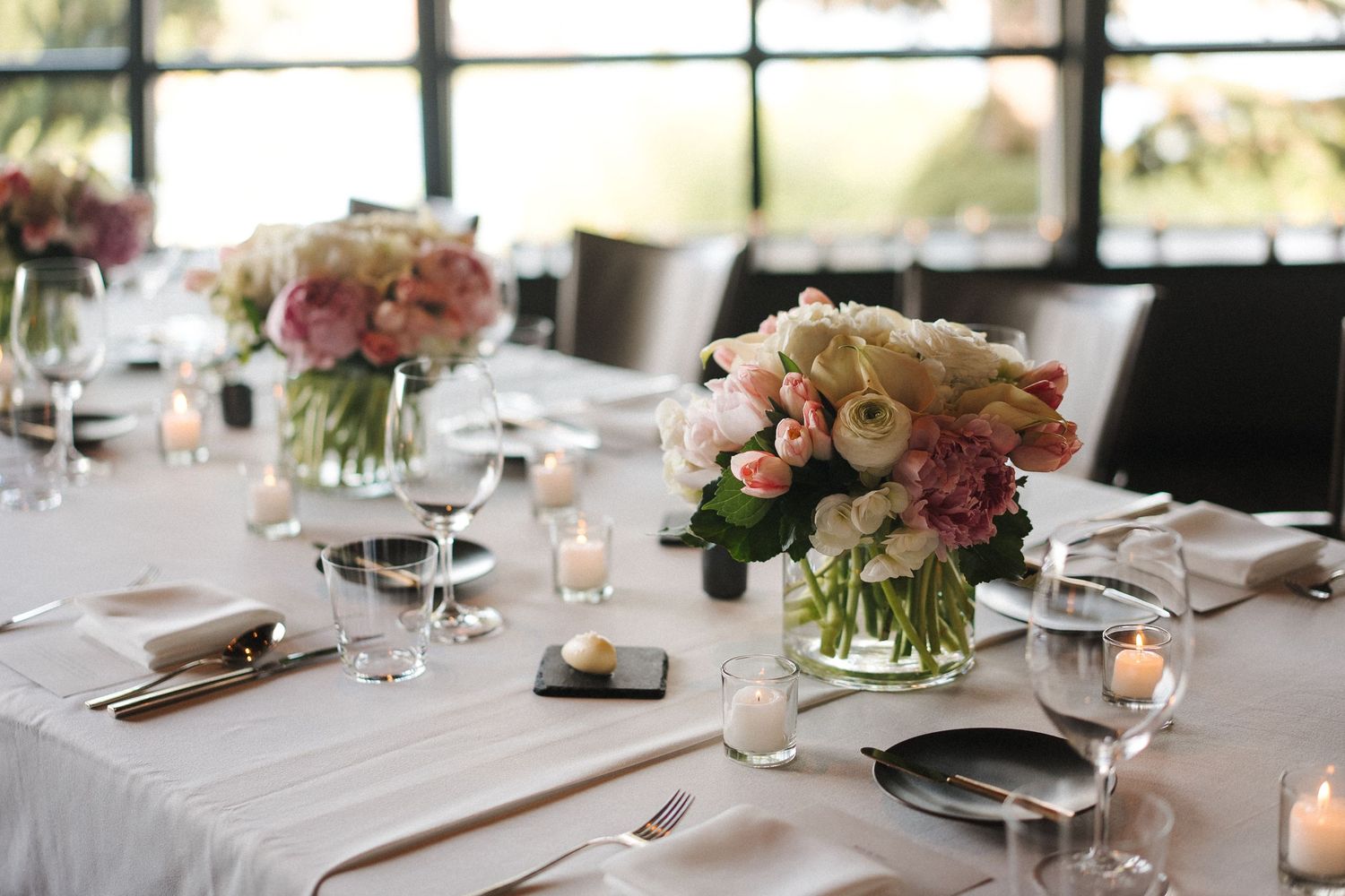 Elegant table settings at a wedding reception with soft pink floral centerpieces and candlelight glowing on white linens.