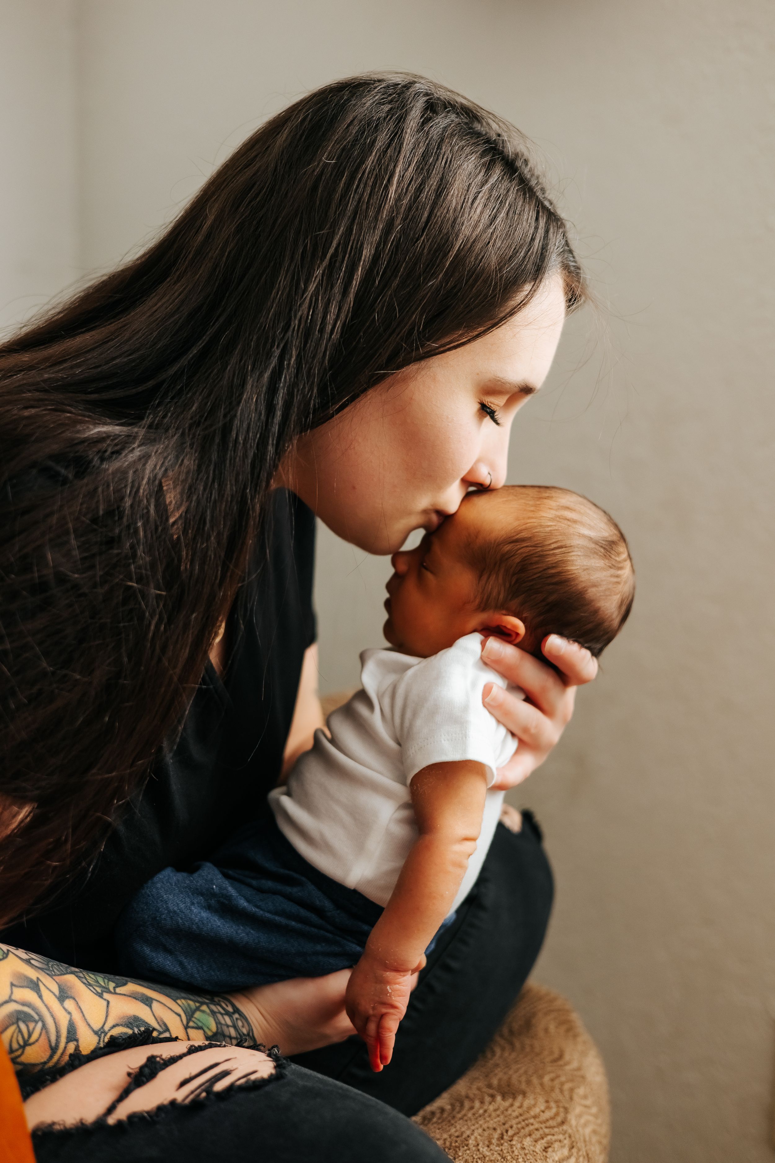 Parent with long dark hair kisses newborn baby during indoor photo session.