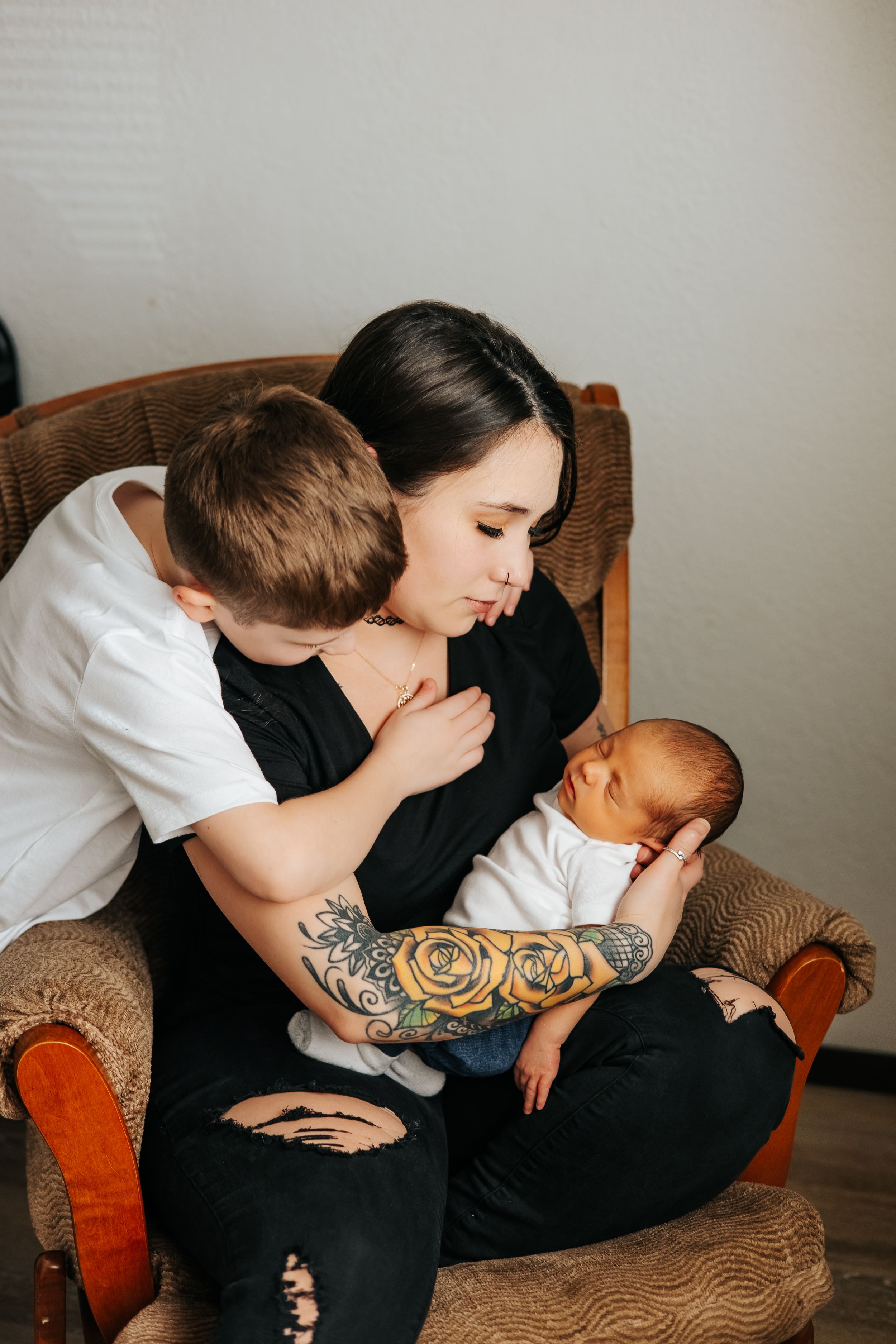 Family of three share intimate moment in brown armchair during newborn photo session.