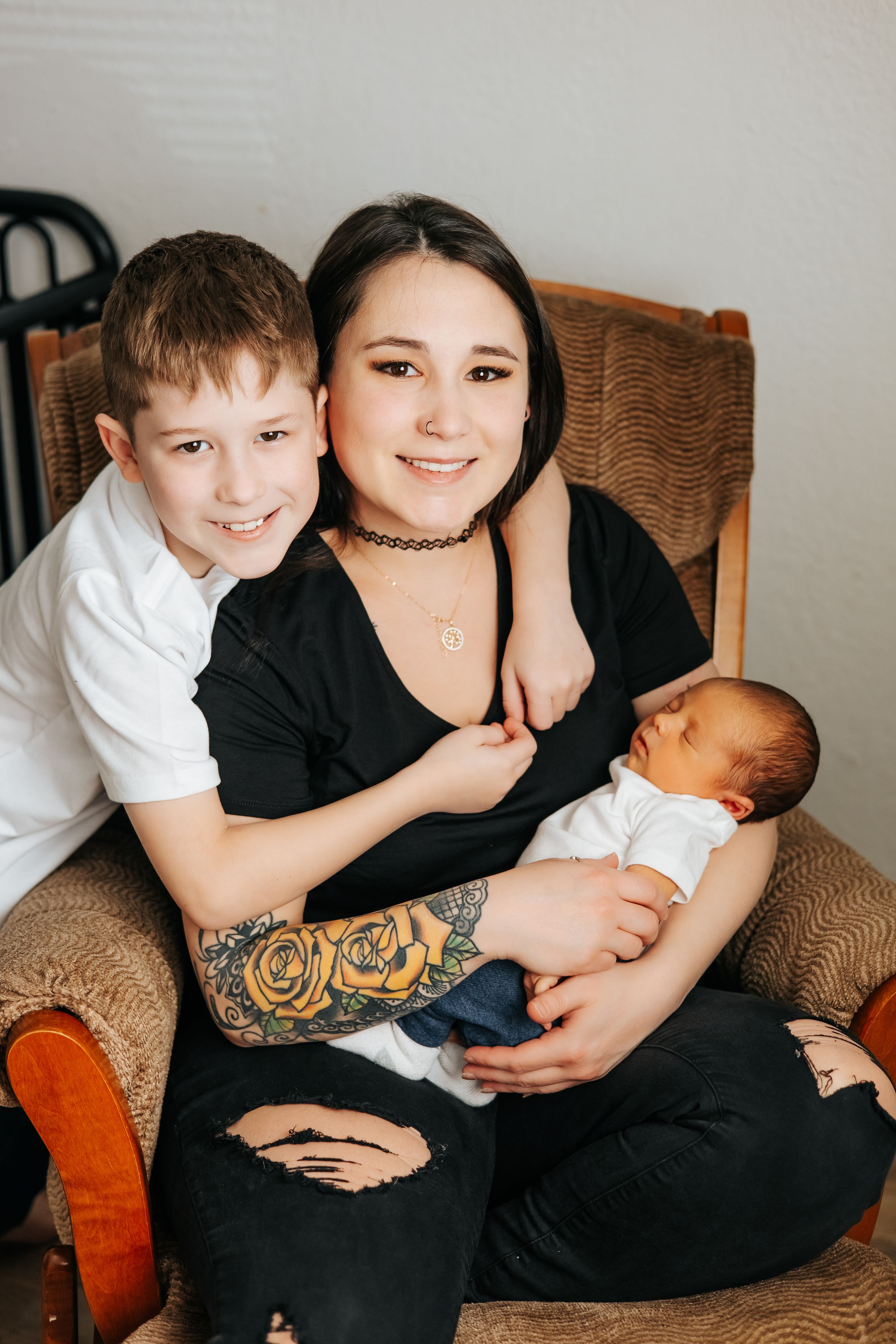 Family portrait showing mother with two children in brown wooden chair.