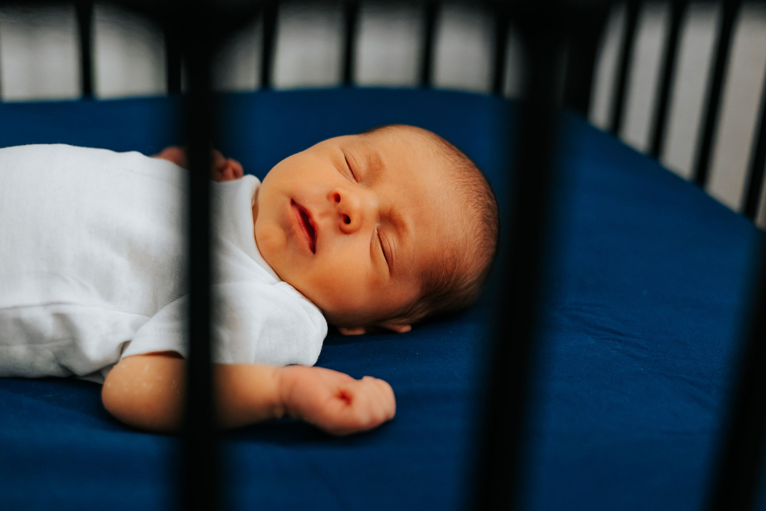 Baby sleeping peacefully in a crib with white bedding and blue background.