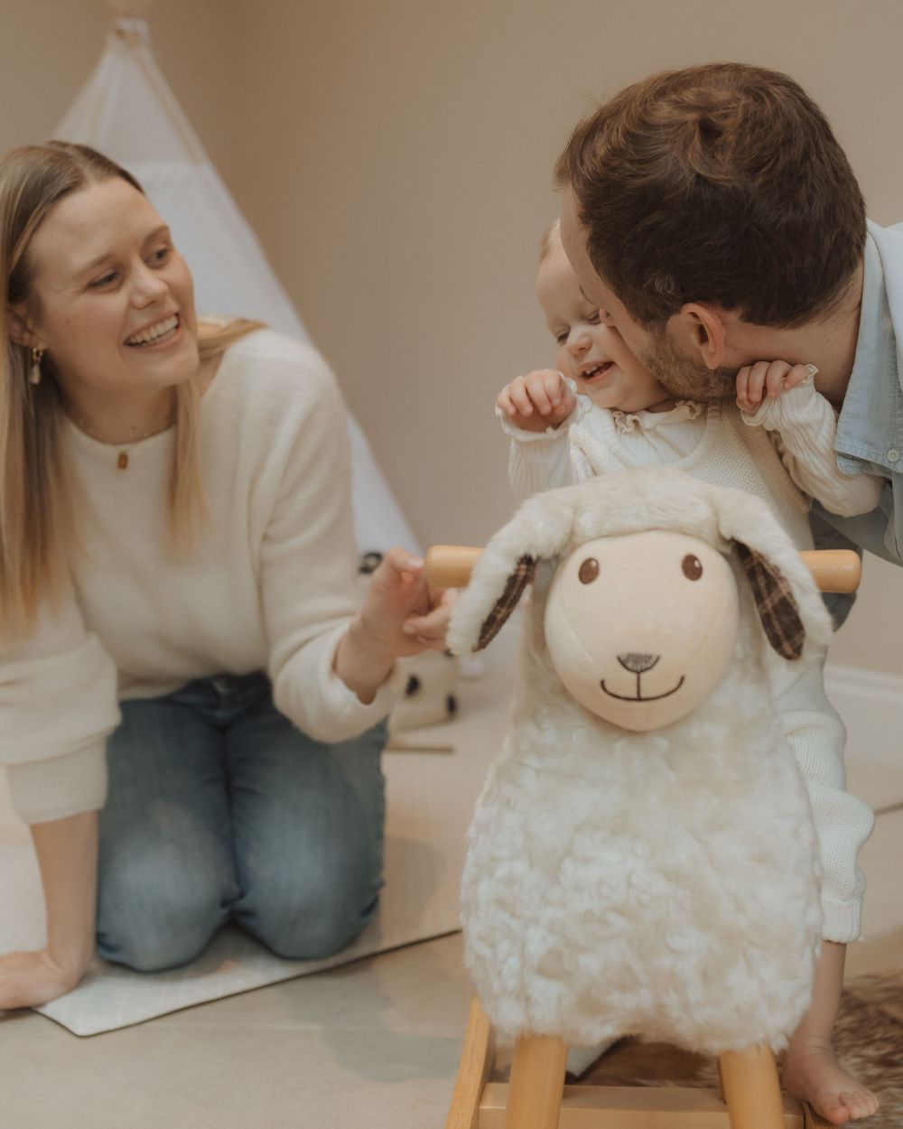Young family spending playful moments together with a plush white rocking sheep toy in a cozy room.
