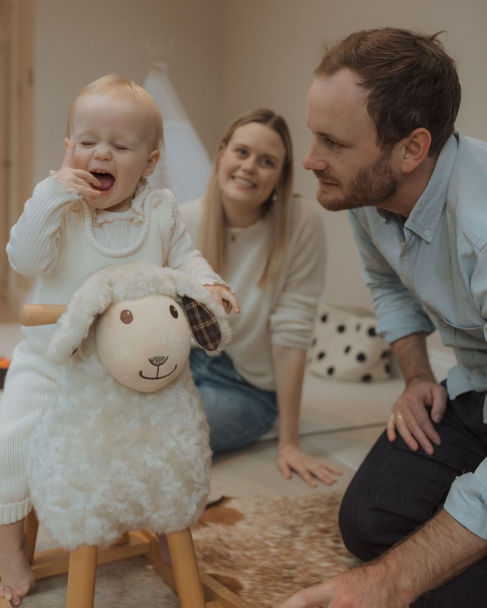 Family enjoys playtime with a plush sheep rocker toy on a carpeted floor in a cozy living room setting.