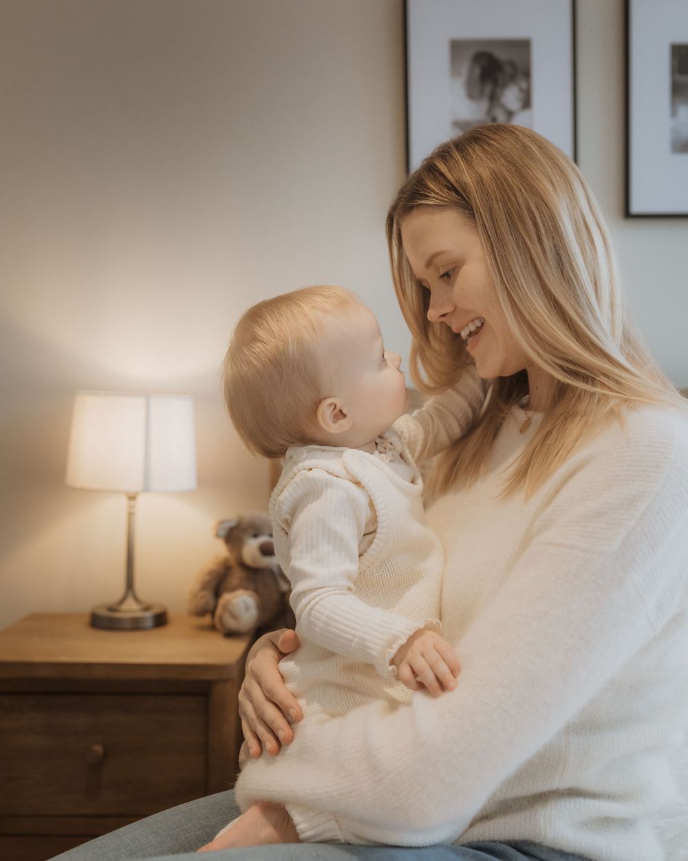 A tender moment of mother and baby sharing laughter and closeness in a cozy bedroom with warm lighting.
