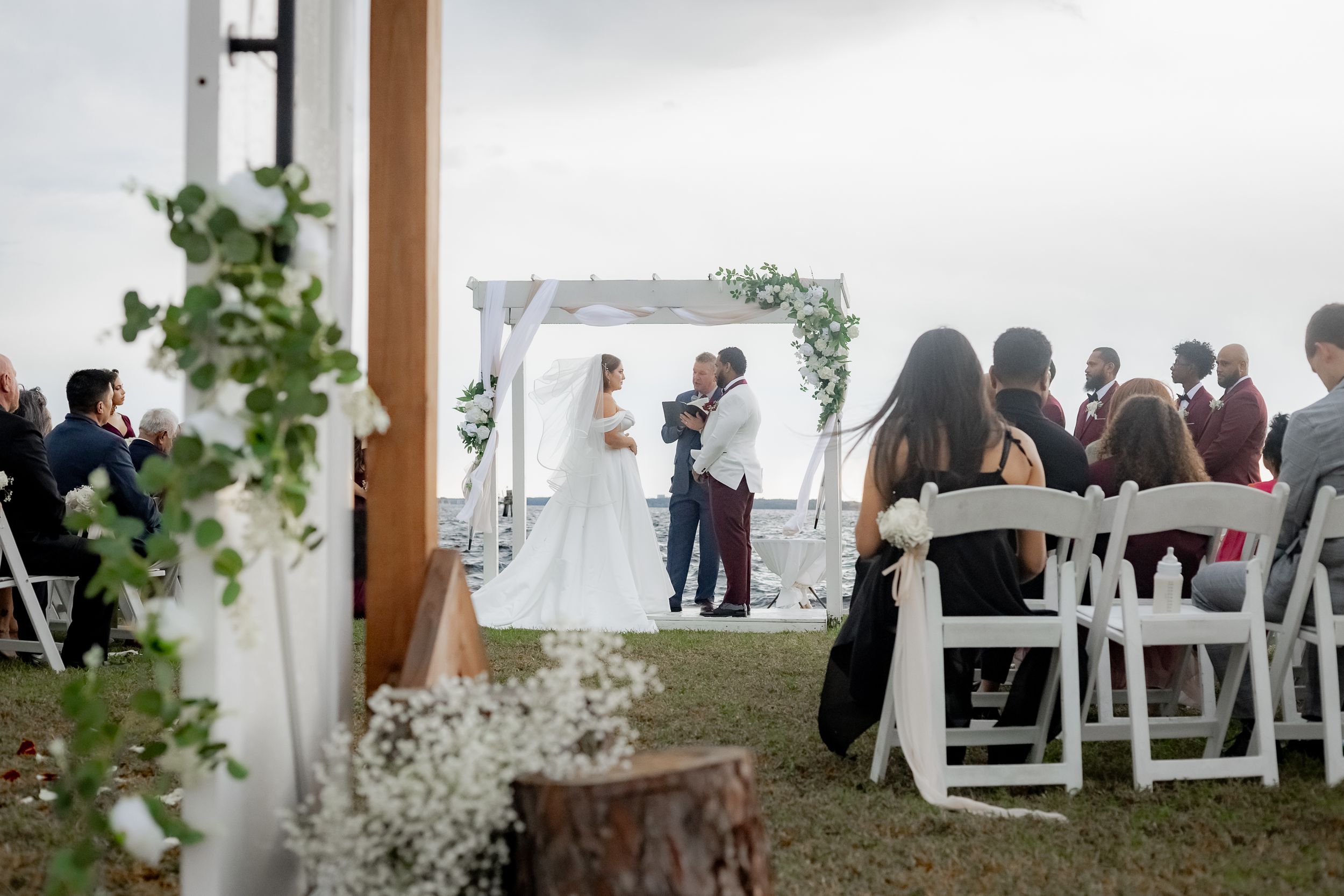 White folding chairs arranged in rows for an outdoor wedding ceremony with greenery and floral decorations.