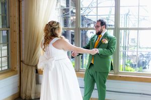 Wedding couple dances and celebrates in sunlit room with large windows.