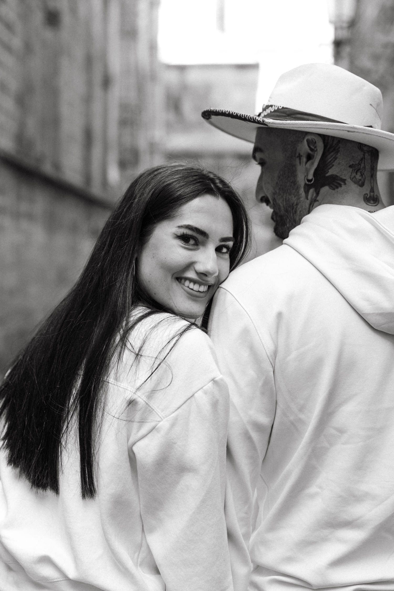 Couple in white outfits sharing playful moments against stone wall background.